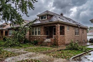 Storm-damaged Chicago brick bungalow with roof damage and fallen tree branches