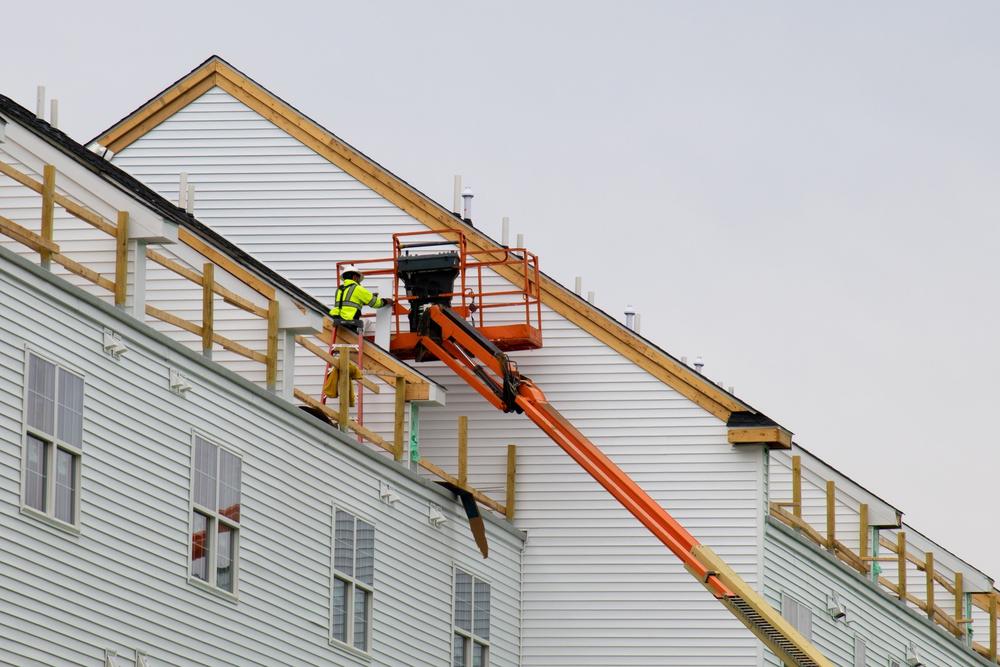 Crew member on a boom lift installing new siding and trim on a multi-story home